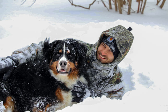 A snow covered man plays with his dog.