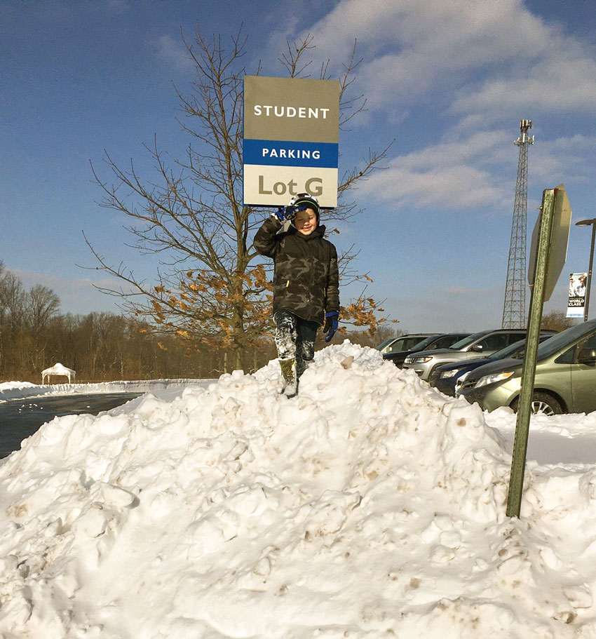 A boy standing on a large pile of of snow.