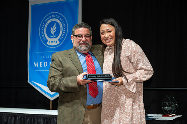 Interim Dean Eugene Mowad hands award to medicine student Whitney Stolnicki in front of College of Medicine banner