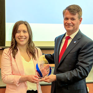 A woman holding a glass award, standing with the university president.