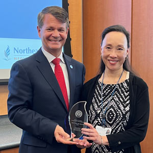 A woman holding a glass award, standing with the university president.