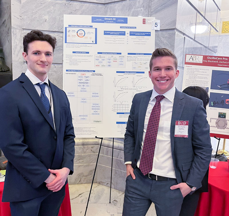 Two students in coats stand with a poster describing their project.
