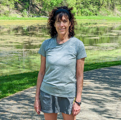 A woman in a gray shirt walking on a hiking trail.