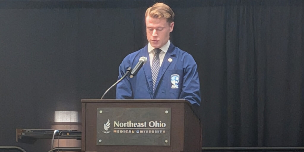 young man wearing a blue jacket and blue striped tie stands at the NEOMED podium