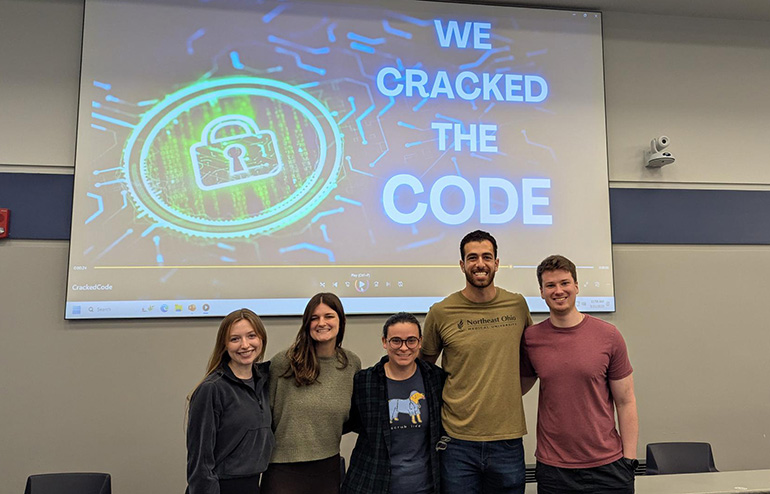 five young people stand below a sign that reads "we cracked the code"