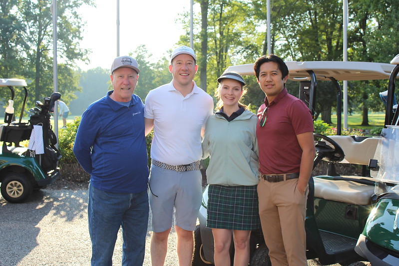 Four golfers pose in front of a golf cart