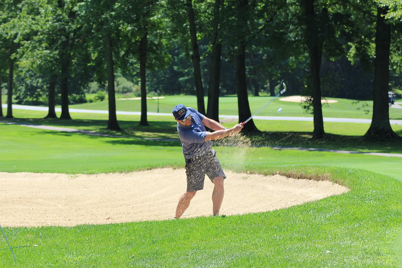 A golfer takes a swing in a sand trap