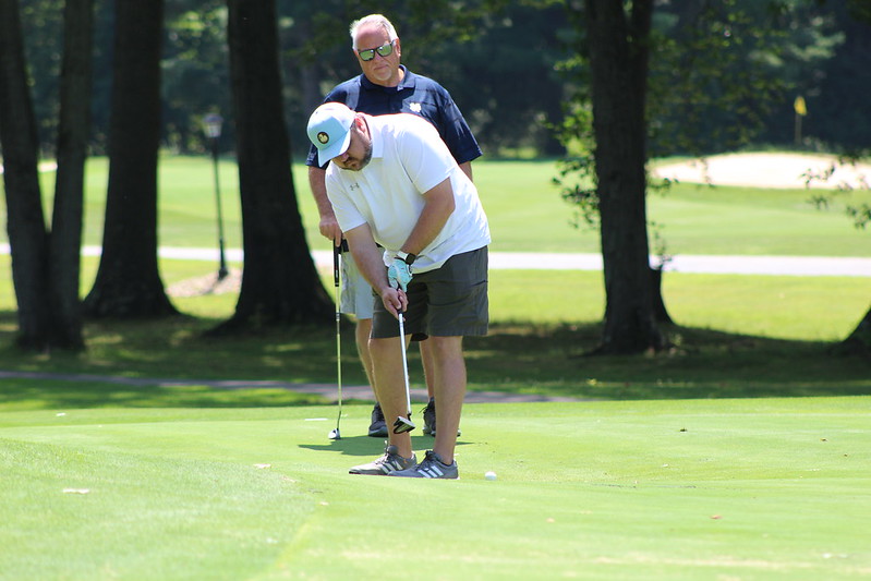 A golfer lines up a shot while a man looks on