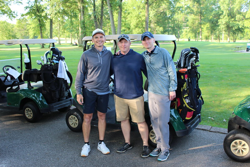 Three golfers pose in front of a golf cart