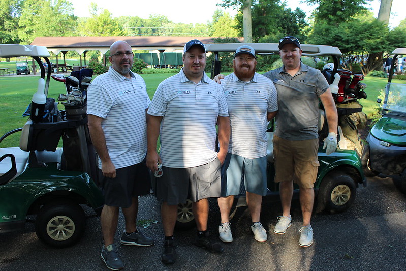 A group of four golfers poses in front of a golf cart