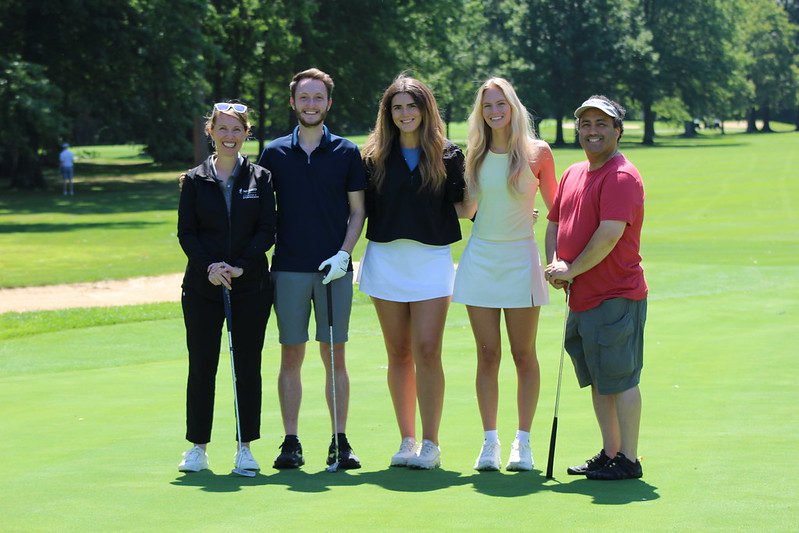 A group of five golfer poses on the green