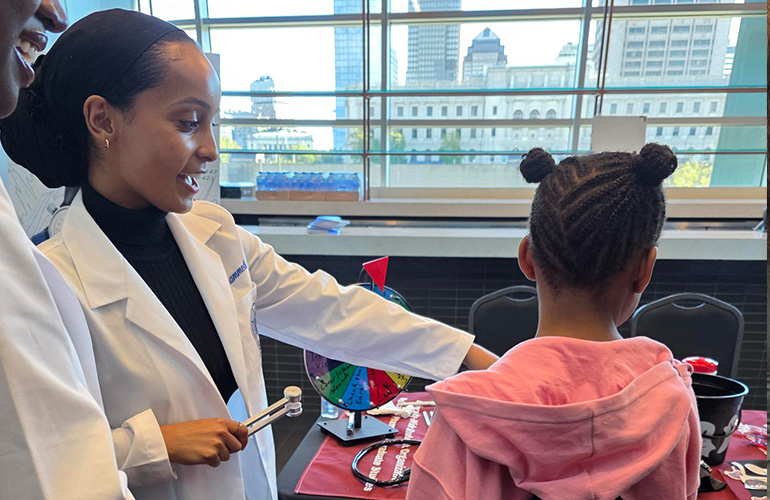 young woman wearing a white coat shares information with a little girl wearing a pink hoodie