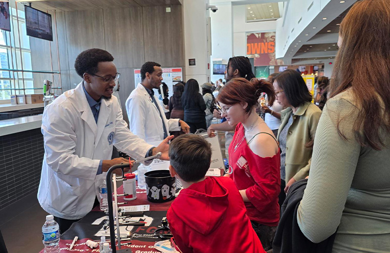 young man wearing a white coat shares information with visitors at a health fair table