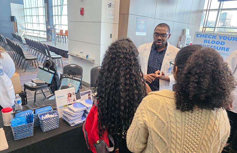 young man in a white coat shares information with visitors to a health fair table