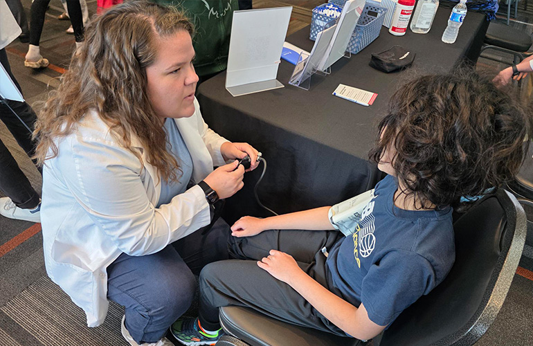 young woman in a white coat stoops down to listen to a seated young child