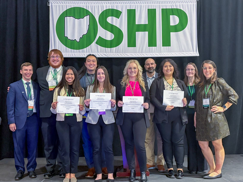 A group of about 10 people stand before a banner that says OSHP.