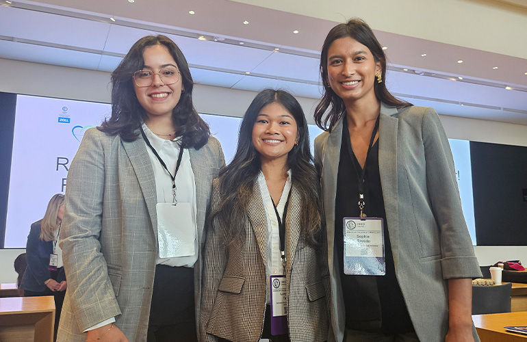 three young women wearing gray jackets and conference lanyards