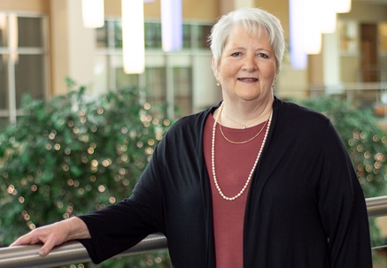 Woman in black sweater and maroon top poses with her arm resting on a railing