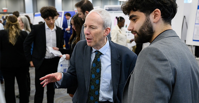 Man in suit and tie talks with a man with a beard 
