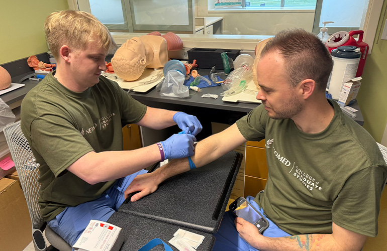 A CAA program student practices giving an IV on another student