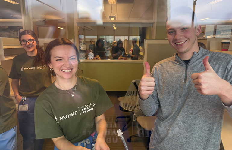 Three students look through a lab window at the photographer
