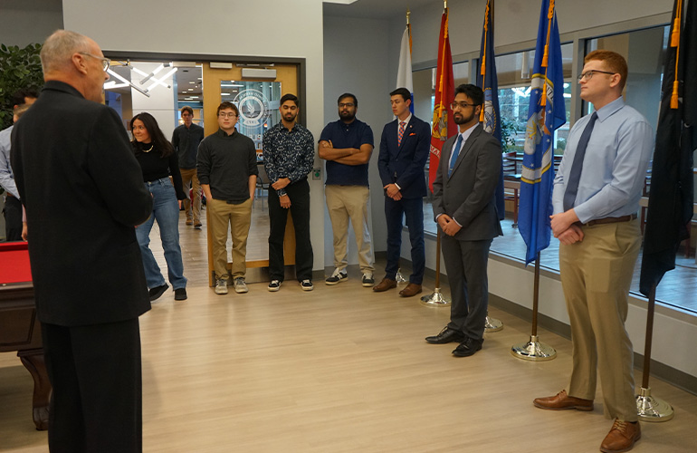 Guests stand in semicircle at commissioning ceremony for two NEOMED students