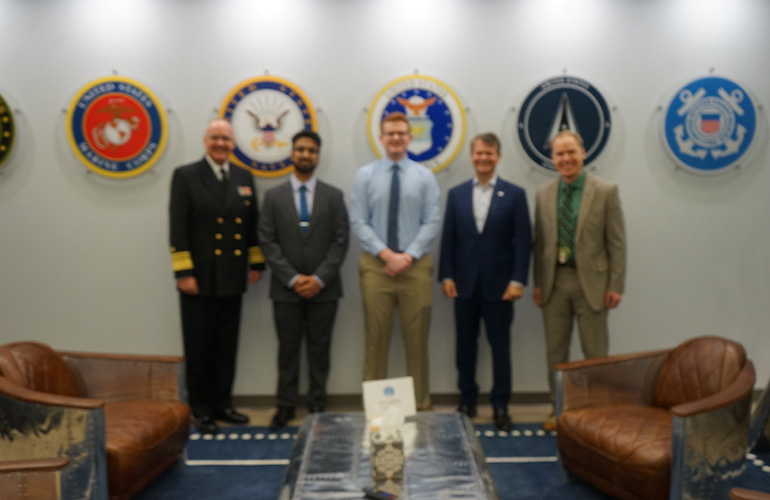 A group of men pose in front of seals representing branches of the U.S. military