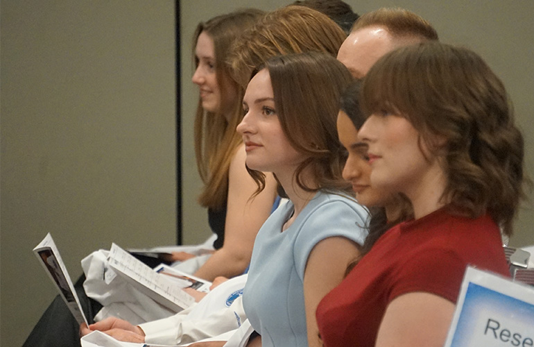 Student graduates smiling while sitting and looking at front of ceremony