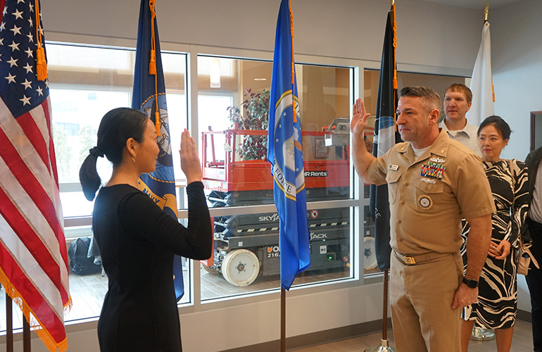 Young woman raises her right hand as she takes an oath administered by a naval officer.