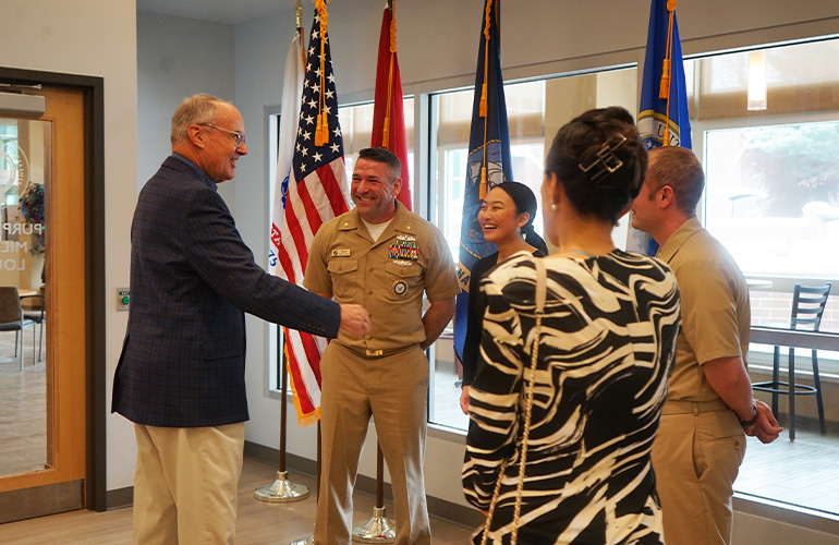 Man in suit extends hand to young woman following a military oath ceremony