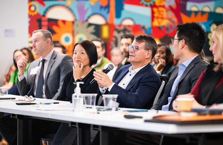 Dr. Langell and UH employees sitting at a table at the Ideator event, looking at the presentation in front of the room