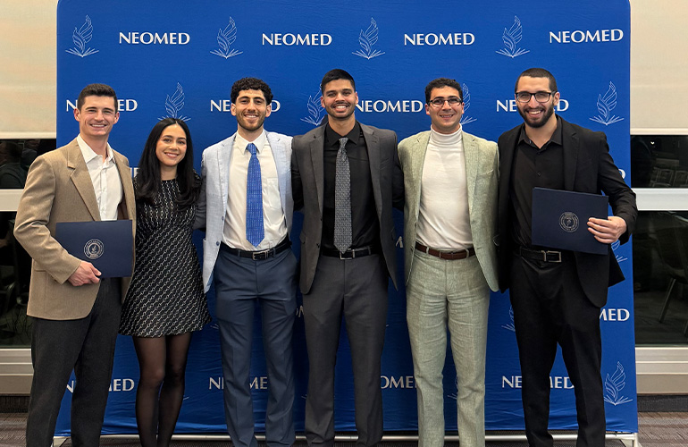 Senior AOA inductees stand together in front of a NEOMED backdrop