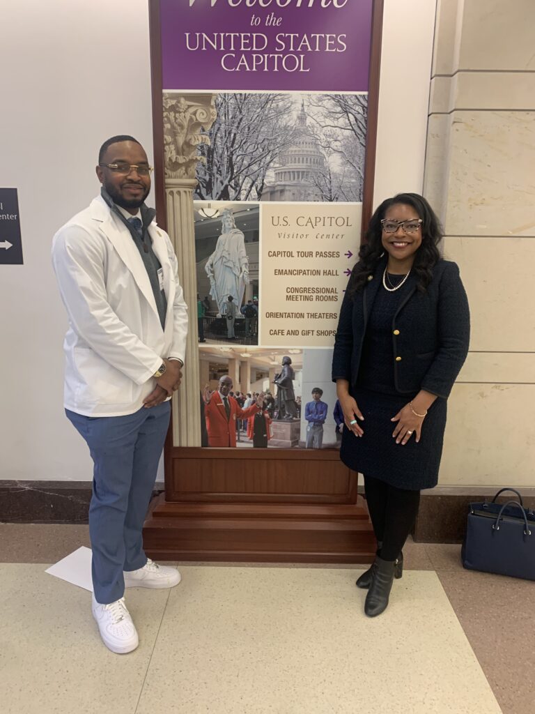 Man in white coat poses with woman in black suite at the U.S. Capitol