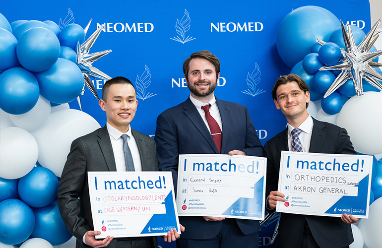 Three young men hold signs saying "I matched" in front of a NEOMED backdrop flanked by blue, white and silver balloons