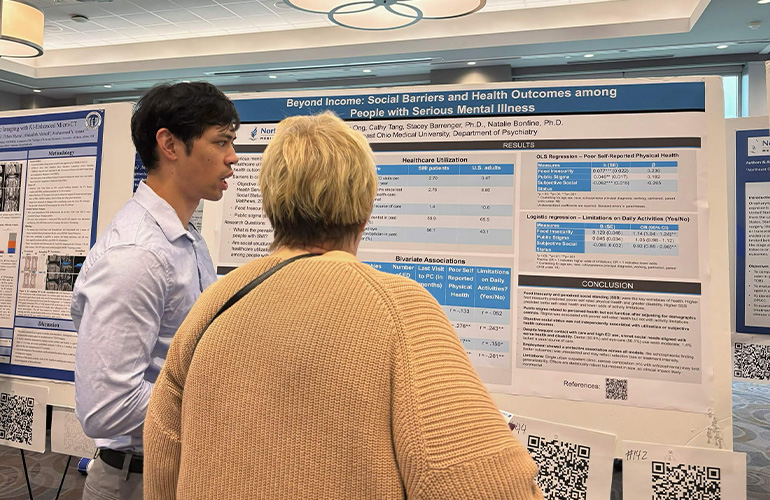 Man in white shirt discusses academic poster with woman with back to the camera