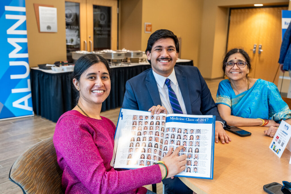 Members of the Brahmandam family seated at a table showing a NEOMED yearbook