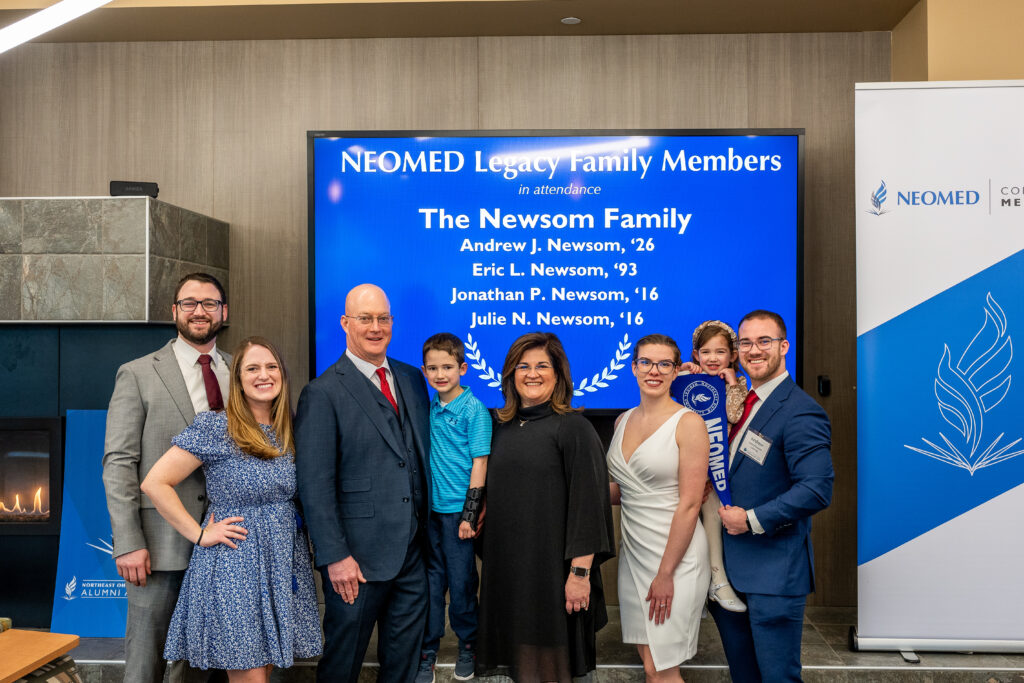 Members of the Newsom family pose in front of a NEOMED backdrop