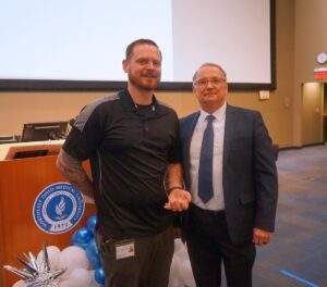 two men pose in front of a podium bearing the NEOMED seal