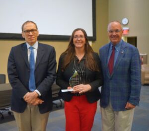 Two men and a women in business attire pose in front of a screen in a large conference hall