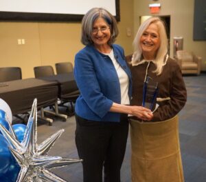 Two women in business attire pose in a large conference hall