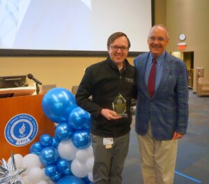 Two men pose next to a podium bearing the NEOMED seal and a display of blue and white balloons