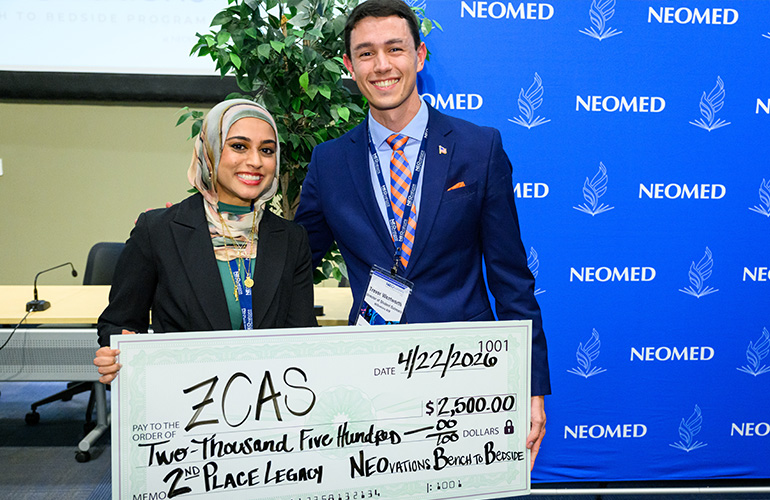 Team ZCAS poses with an oversized check in front of a blue NEOMED backdrop