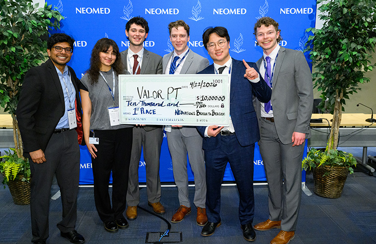Team ValorPT pose with an oversized check for $10,000 in front of a blue NEOMED backdrop