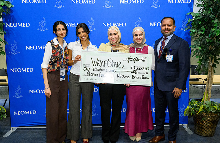 Team Wrap Star poses with an oversize check for $2,000 in front of a blue NEOMED backdrop