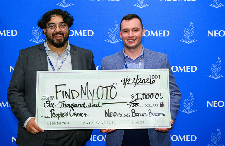 Team FindMyOTC poses with an oversized check for $1,000 in front of a blue NEOMED backdrop