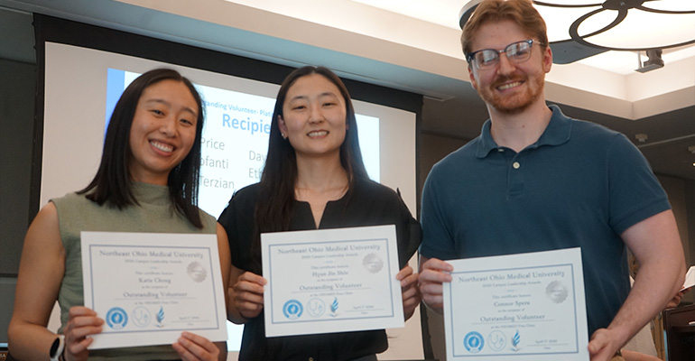 Two women and a man pose with award certificates