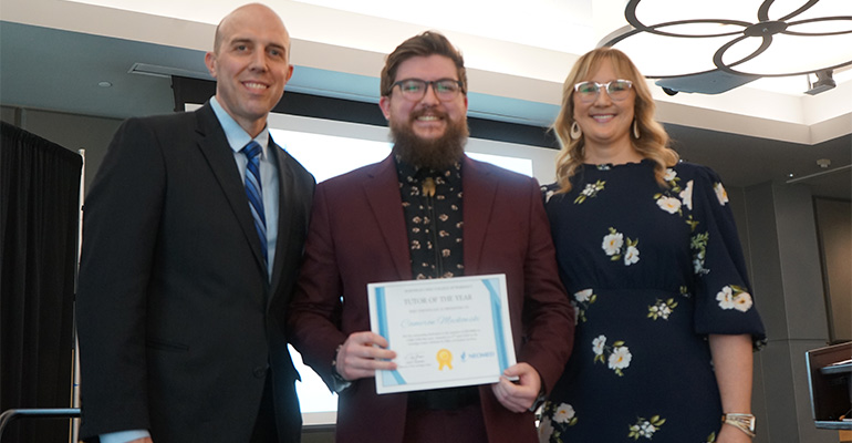 Two men and a women smile at the camera. The man in the center holds an awards certificate