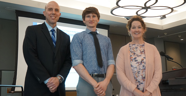 Two men and a woman stand in a line and smile at the camera