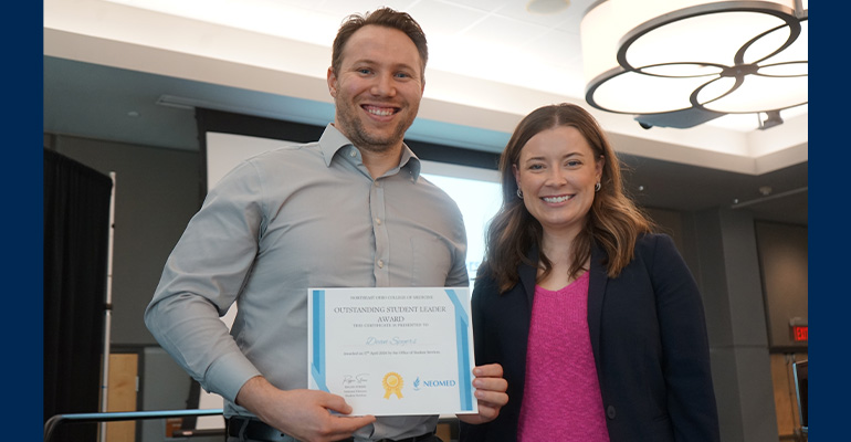A man holding an awards certificate stands next to a woman in a pink shirt and black sweater