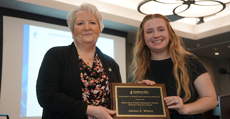 Two woman pose for a photo holding a wooden award plaque